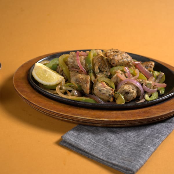 Chicken and vegetable fajitas on a cast iron platter with lime and two dipping sauces.