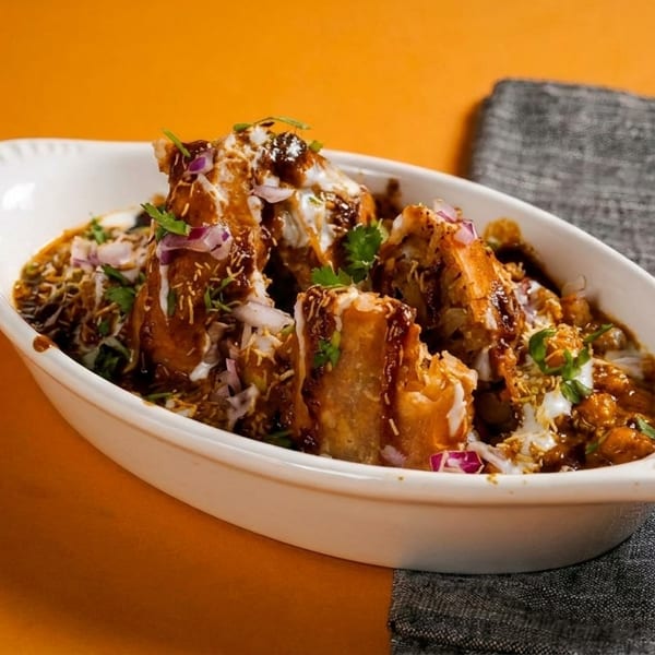 Savory Indian dish topped with sauces, yogurt, onions, and cilantro in a white bowl.
